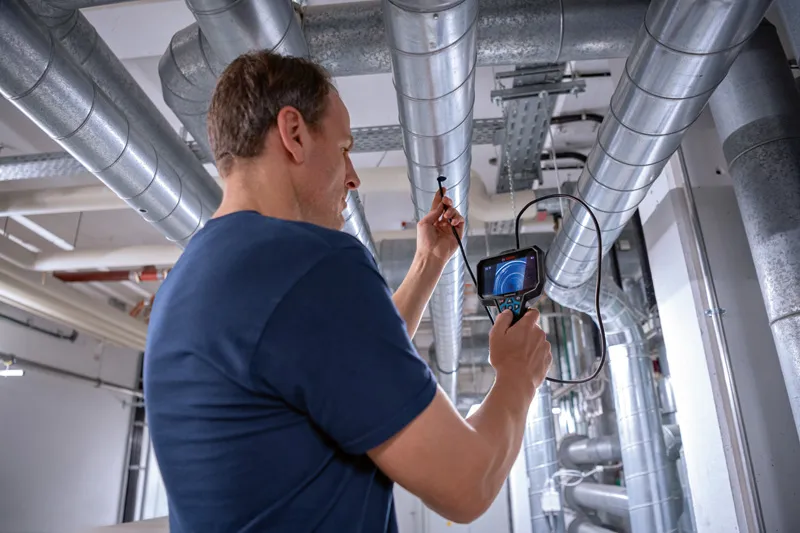 GIC 5-27 C A person inspects overhead pipes using an inspection camera in an industrial setting.