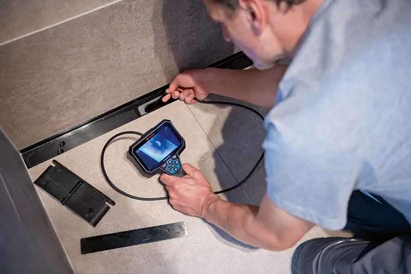 GIC 5-27 C A person uses an inspection camera to check behind a panel on a tiled wall.