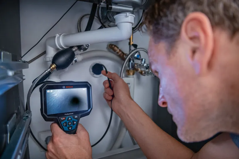 GIC 5-27 C A person inspects plumbing under a sink using an inspection camera.