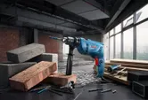 Impact drill with drill bits rests on a worktable surrounded by bricks and wood in a construction area.
