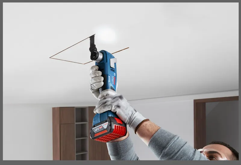 GOP 185-LI A person wearing safety equipment cuts a ceiling panel with a cordless multi-cutter.