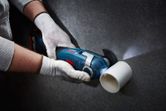 A person wearing safety equipment cuts a white plastic pipe with a cordless multi-cutter.