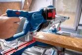 Person cuts a wooden board with a cordless mitre saw on a workbench.