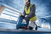 A person wearing safety equipment uses a cordless concrete nailer on a construction floor.