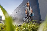 A person wearing safety equipment trims tall grass with a cordless grass trimmer.