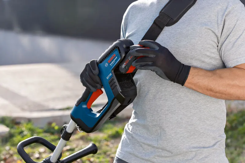 A person wearing safety equipment attaches a battery to a cordless grass trimmer.