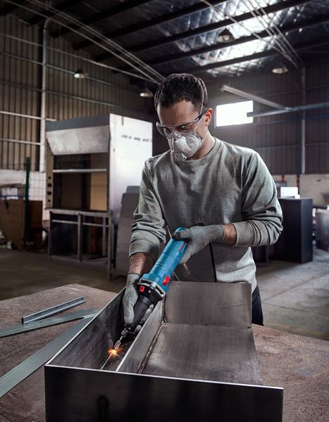 A person wearing safety equipment grinds metal inside an industrial workshop.