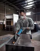 A person wearing safety equipment grinds metal inside an industrial workshop.