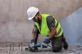 A person wearing safety equipment cuts exposed rebar with an angle grinder.