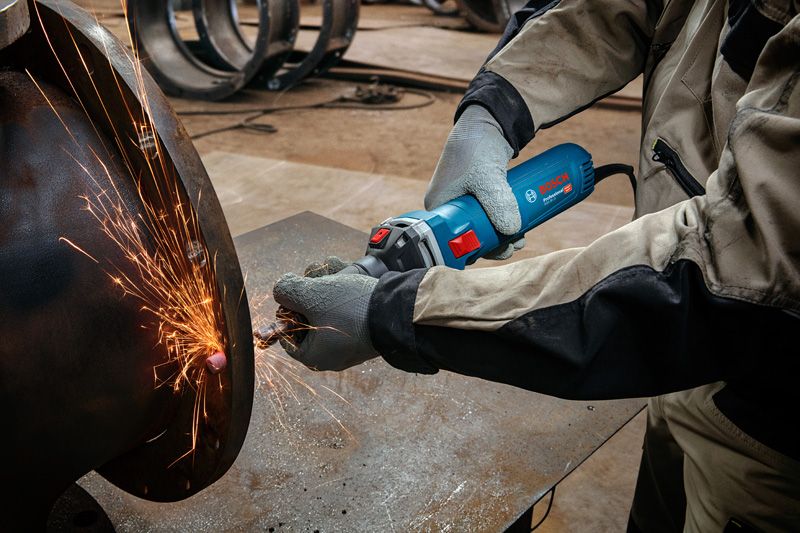 A person wearing safety equipment grinds metal, creating bright sparks.
