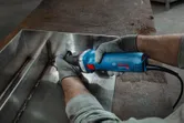 A person wearing safety equipment grinds a welded metal seam with a straight grinder.