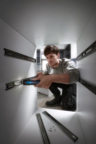 Bosch GO A person uses a cordless screwdriver to install drawer slides inside a cabinet.