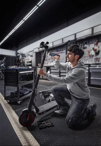 Bosch GO A person repairs an electric scooter using a cordless screwdriver in a workshop.
