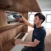 A person secures wires in an electrical panel using a cordless screwdriver.