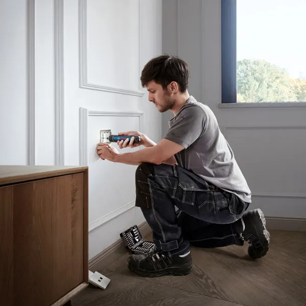 Bosch GO A person uses a cordless screwdriver to install an electrical outlet cover.