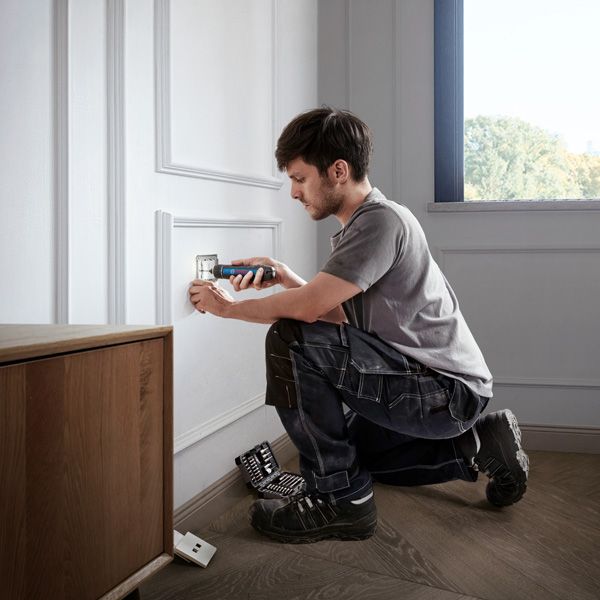 A person uses a cordless screwdriver to install an electrical outlet cover.