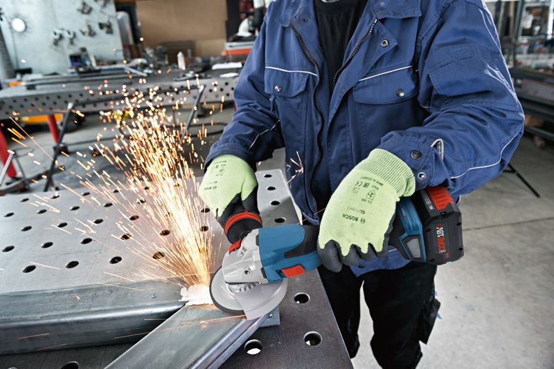ProCORE18V+ 8.0Ah A person wearing safety equipment grinds metal with a cordless angle grinder, causing sparks.