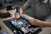 Person using a cordless screwdriver to assemble a laptop on a workbench.