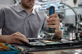 Person using a cordless screwdriver to assemble electronic components on a circuit board.