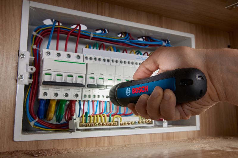Person using a cordless screwdriver to tighten screws on an electrical panel.