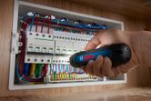 Person using a cordless screwdriver to tighten screws on an electrical panel.