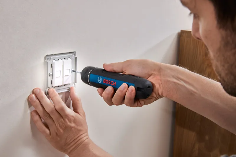 Bosch GO A person uses a cordless screwdriver to fasten screws on a light switch panel.