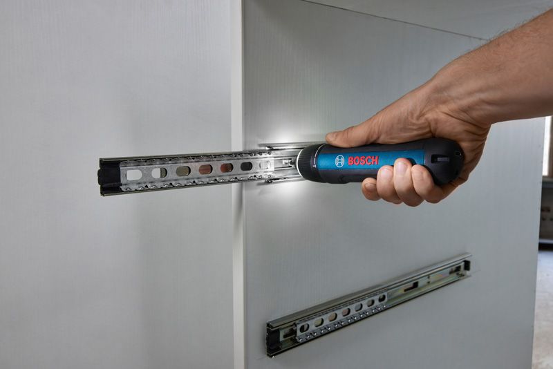 Bosch GO A person uses a cordless screwdriver to install a drawer runner on white cabinetry.