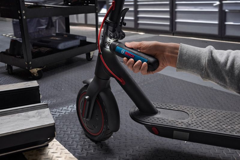 A person uses a cordless screwdriver to adjust the handlebar of an electric scooter.