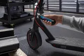 A person uses a cordless screwdriver to adjust the handlebar of an electric scooter.