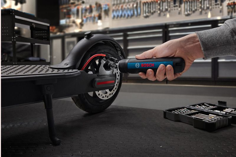 A person uses a cordless screwdriver to tighten a bolt on an electric scooter wheel.
