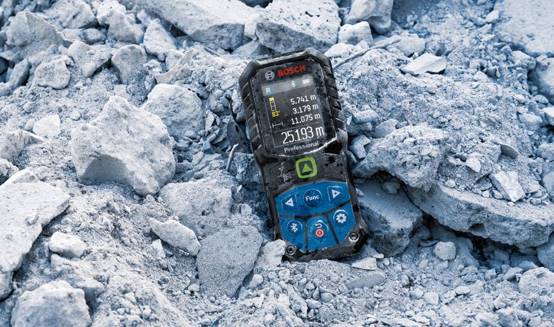 GLM 50-27 CG Laser measure displaying distance values lies on rough construction debris.