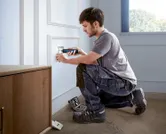 A person uses a cordless screwdriver to install an electrical outlet cover.