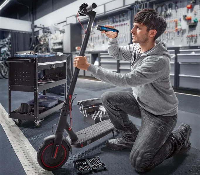 Bosch GO A person repairs an electric scooter using a cordless screwdriver in a workshop.
