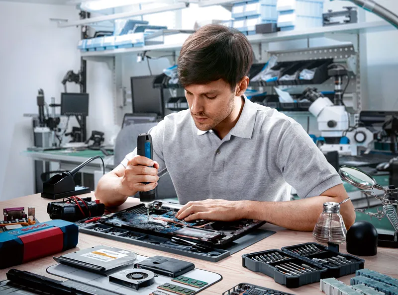Bosch GO A person uses a cordless screwdriver to assemble electronic components on a workbench.