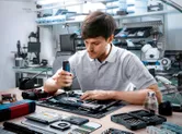 A person uses a cordless screwdriver to assemble electronic components on a workbench.