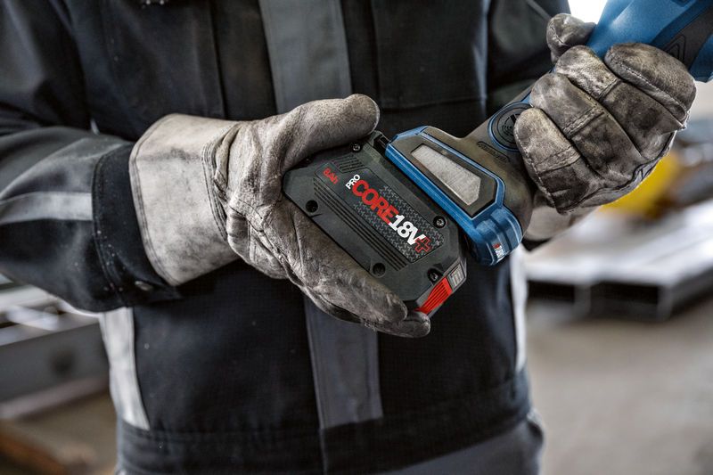 A person wearing safety equipment installs a battery pack onto a cordless power tool.