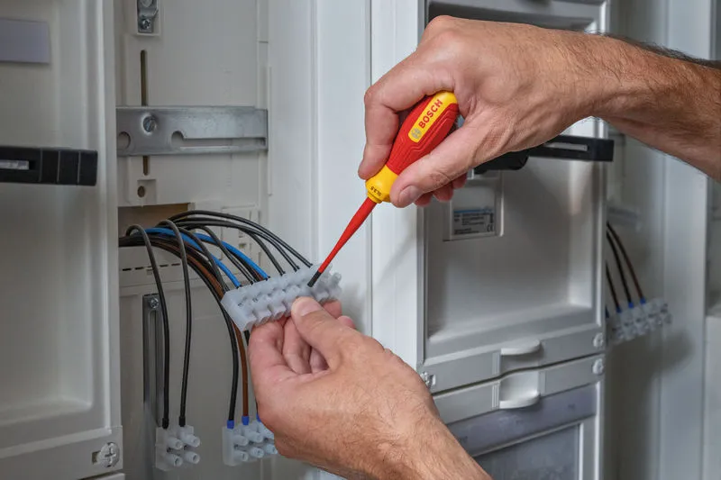 A person uses an insulated screwdriver to tighten wires in an electrical panel.