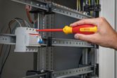 A person tightens a terminal screw on an electrical panel with an insulated screwdriver.