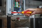 Person using an insulated screwdriver to adjust wiring in an electrical panel.