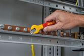 A person tightens a bolt on a copper busbar using an insulated wrench.