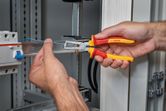 Person strips insulation from a blue wire in an electrical cabinet.
