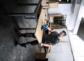 A person wearing safety equipment cuts wood with a power tool in a workshop.