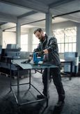 A person wearing safety equipment uses a jigsaw to cut sheet metal in a workshop.