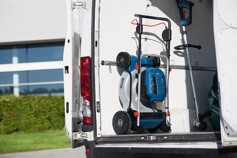 Folded cordless lawnmower and trimmer stored in the back of a white work van.