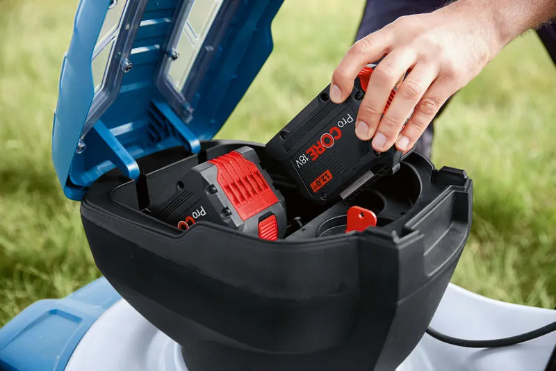 A person inserts a battery pack into a cordless lawnmower outdoors.