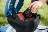 A person inserts a battery pack into a cordless lawn mower outdoors.