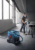 A person wearing safety equipment cuts material with a saw connected to an all-purpose extractor.