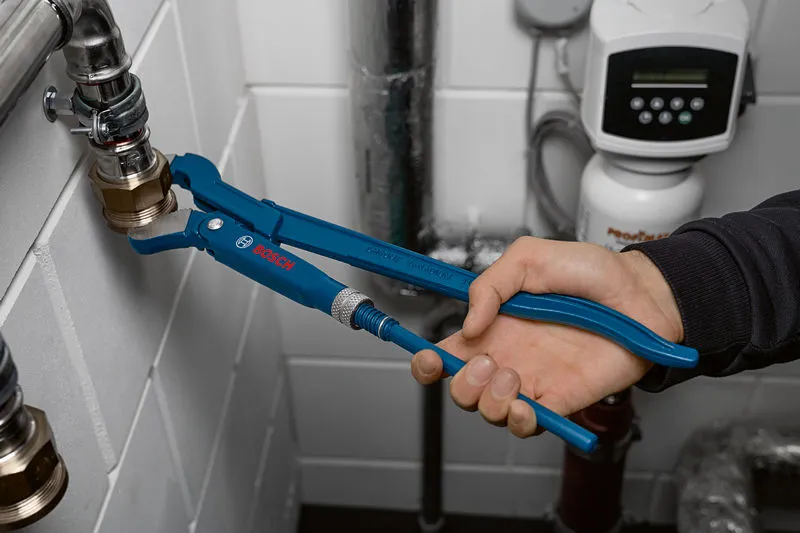 A person adjusts a metal pipe fitting using blue adjustable pliers.
