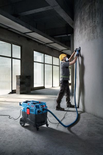 A person wearing safety equipment grinds a concrete wall using an all-purpose extractor.