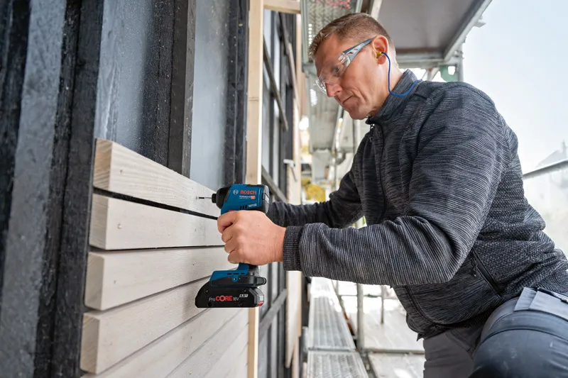 GDR 18V-220 C A person wearing safety equipment uses a cordless drill to fasten wooden boards outdoors.